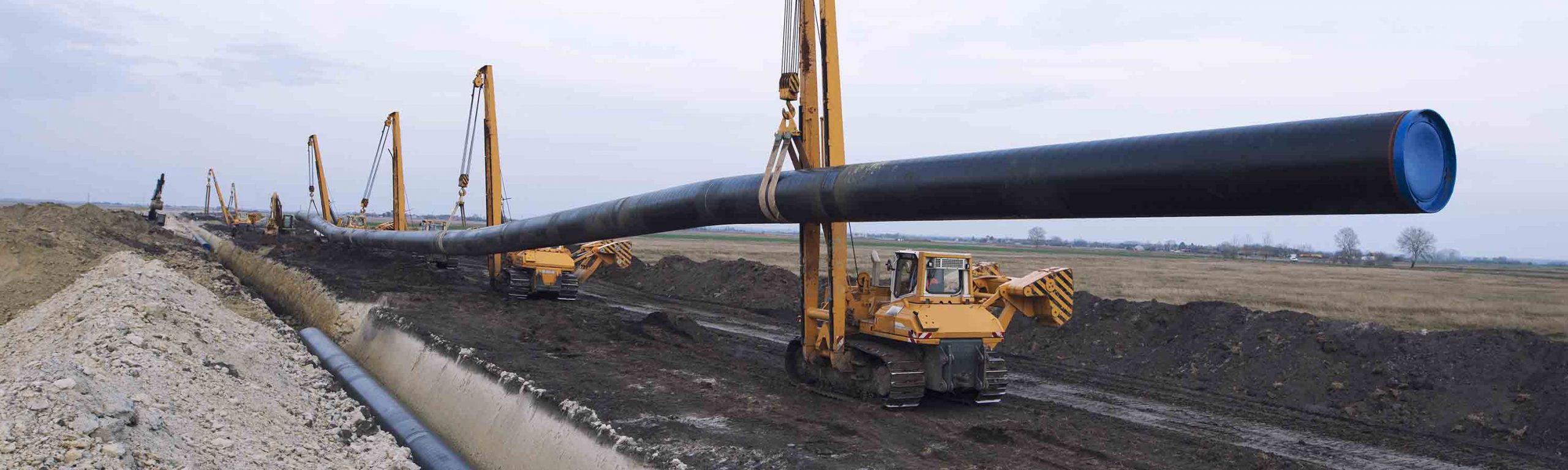 Heavy duty construction machines carrying and placing gas pipe into the ground.